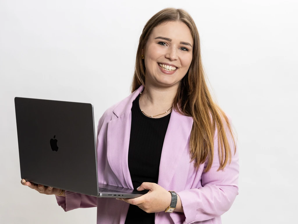 Porträt von Maren Dinges (Copywriting & Content-Strategie, Content mit Maren), vor weißem Hintergrund, mit Laptop in der Hand und lila Blazer.
