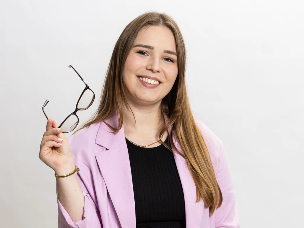 Porträt von Maren Dinges (Social Content und Content-Management, Content mit Maren), vor weißem Hintergrund, mit Brille in der Hand und lila Blazer.