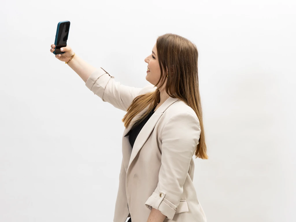 Porträt von Maren Dinges (Content mit Maren), vor weißem Hintergrund, mit Smartphone in der Hand und lila Blazer beim Erstellen von organischem Content.
