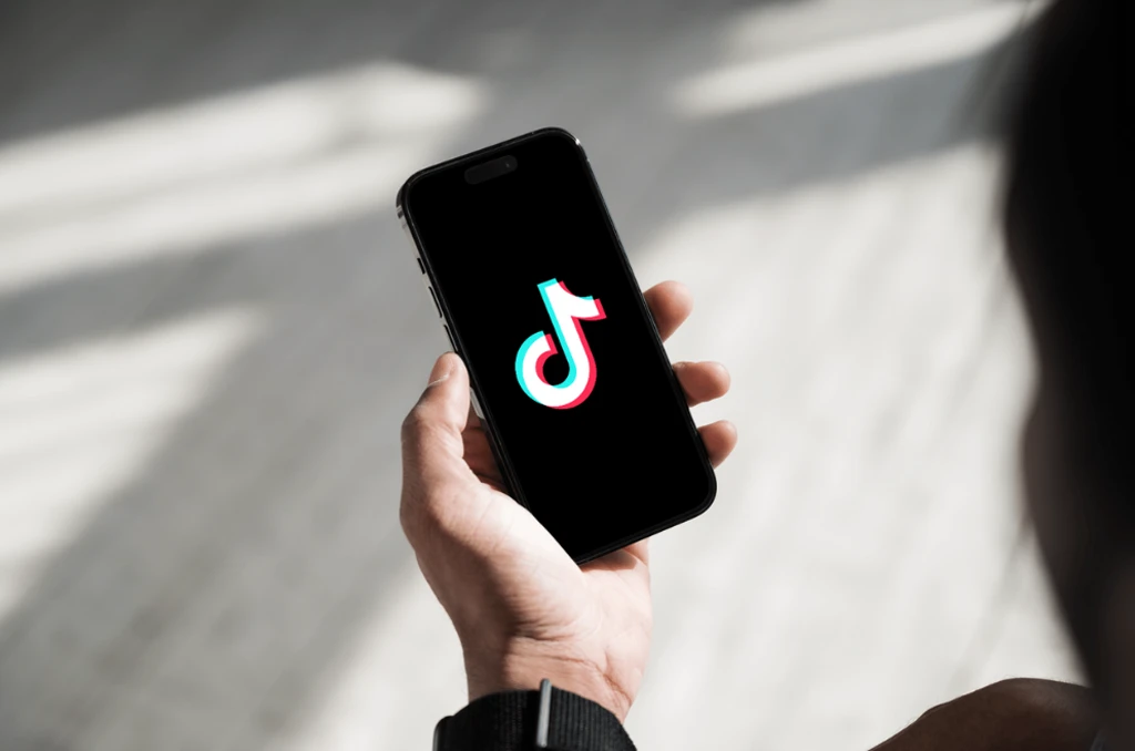 Mensch hält Handy in der Hand mit Tiktok Logo uaf dem Bildschirm